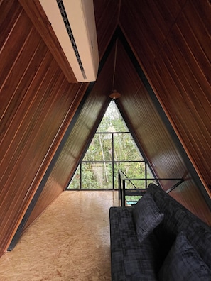 Un dormitorio en ático con paredes de madera, una ventana y un sofá.