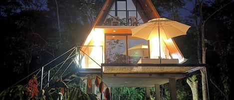 A triangular-roofed building with a balcony, surrounded by greenery.