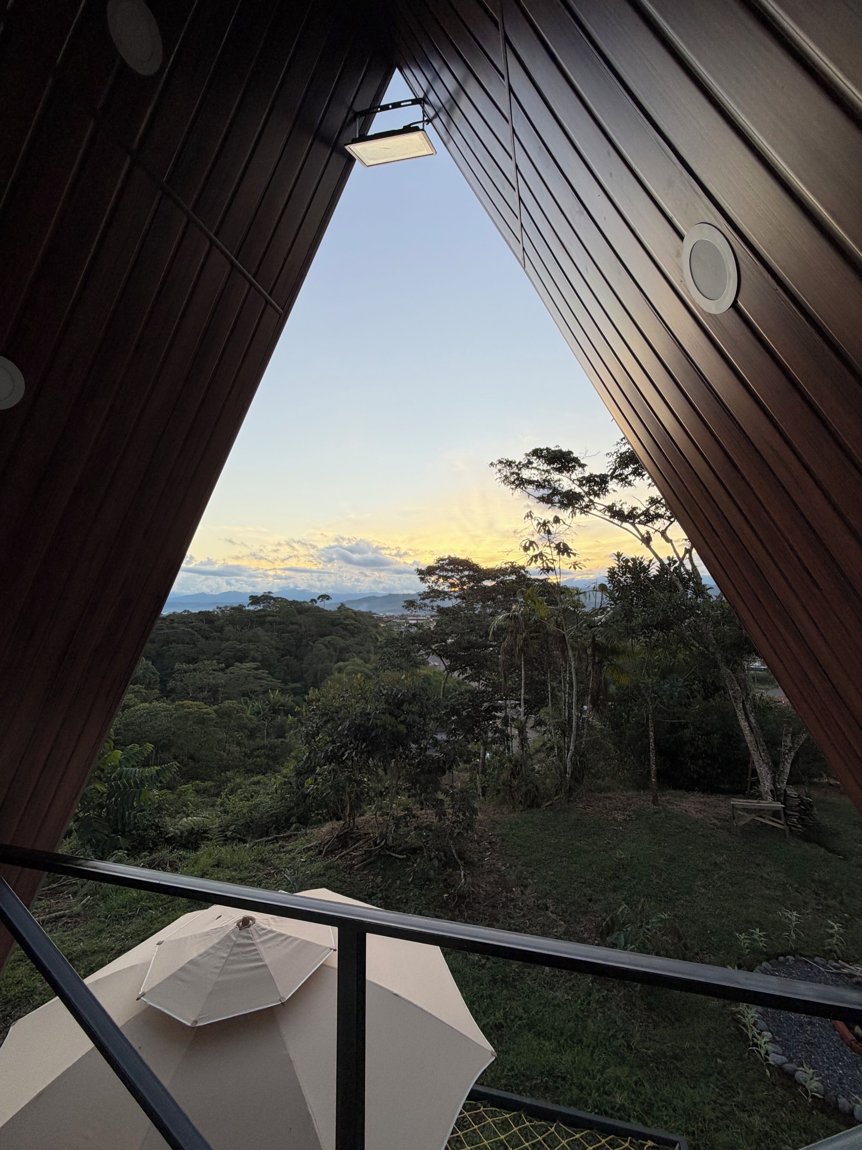 A balcony with a view of a forested landscape and a sunset.