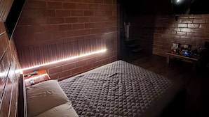 A room with a bed, a brick wall, and a television. - Refugio de la Niebla Puyo Glamping (Puyo)