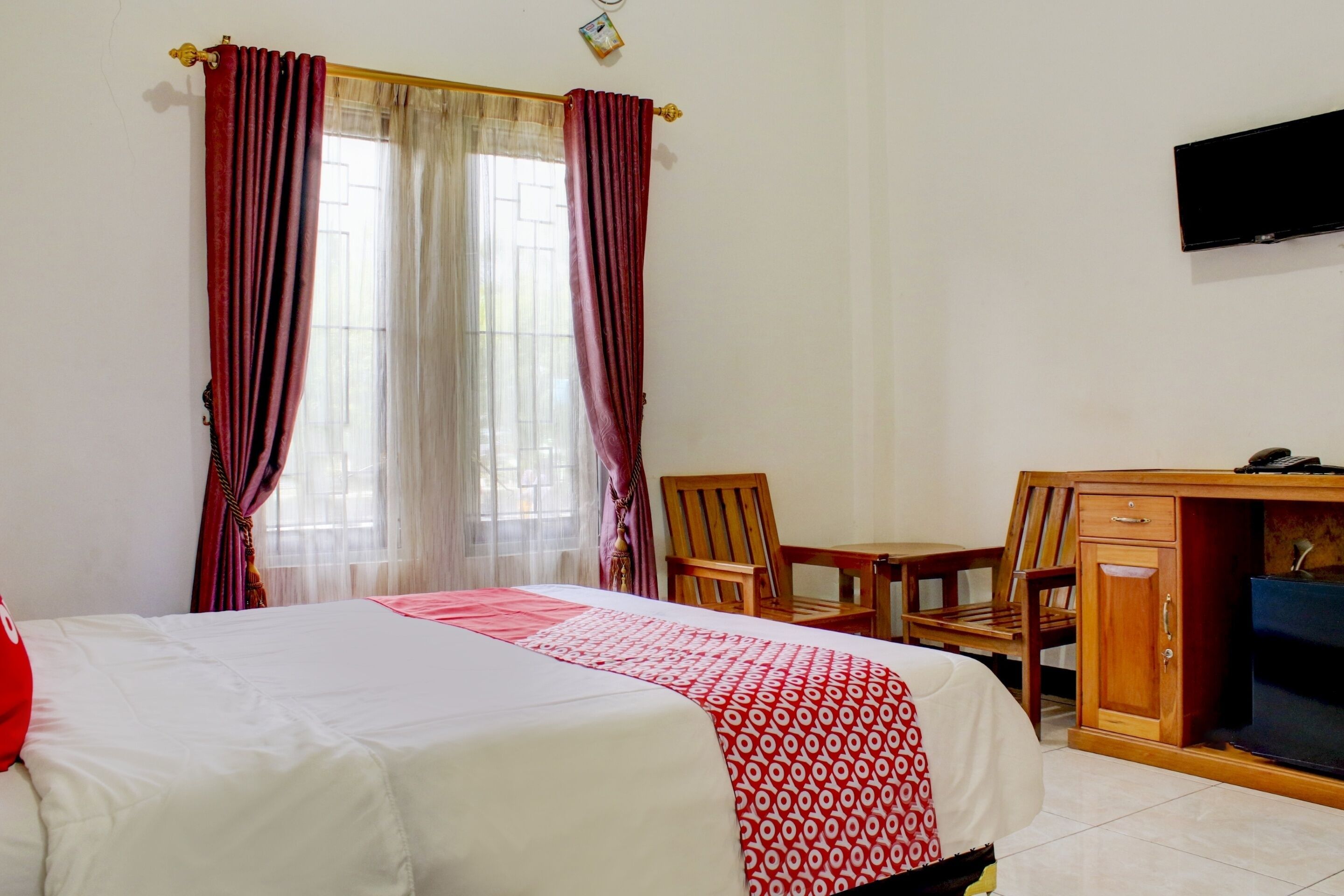 Habitación de hotel con cama, escritorio, silla, televisor y ventana con cortinas.