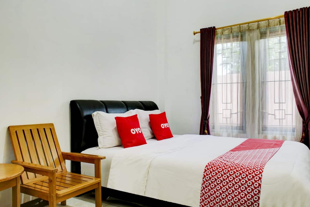 A hotel room with a bed, a wooden chair, and a window with curtains.