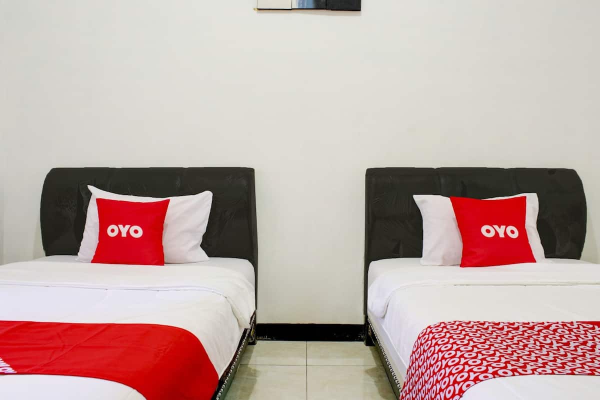 A room with two beds, each with a white mattress and a red pillow with 'OYO' branding.