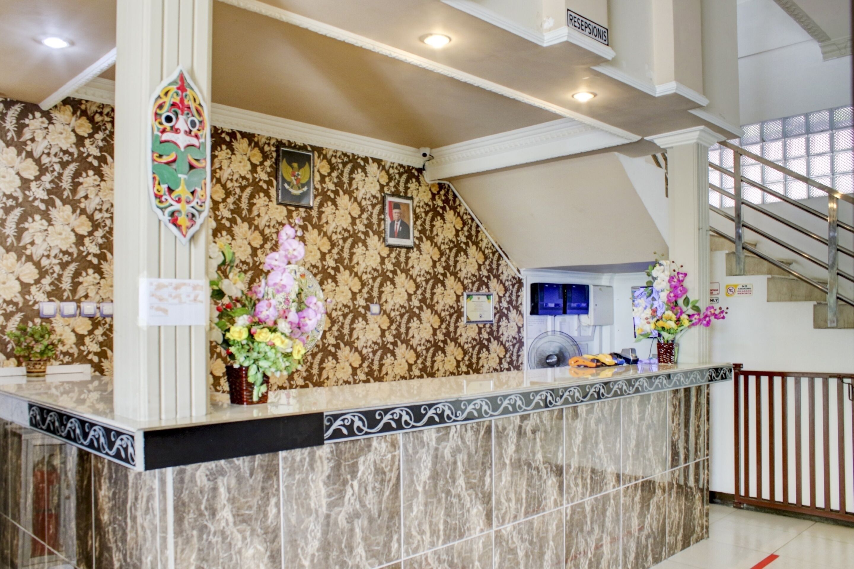 A reception desk with a floral wallpaper, a clock, and a staircase in the background.