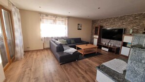 A living room with a sofa, a coffee table, a TV, and a stone wall. - Large vacation apartment with garden (Lauda-Königshofen)