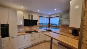 A modern kitchen with white cabinets, a built-in stove, a sink, and a window with curtains. - Large vacation apartment with garden (Lauda-Königshofen)