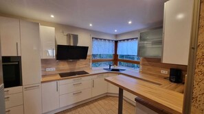 A modern kitchen with white cabinets, a built-in stove, a sink, and a window with curtains. - Large vacation apartment with garden (Lauda-Königshofen)