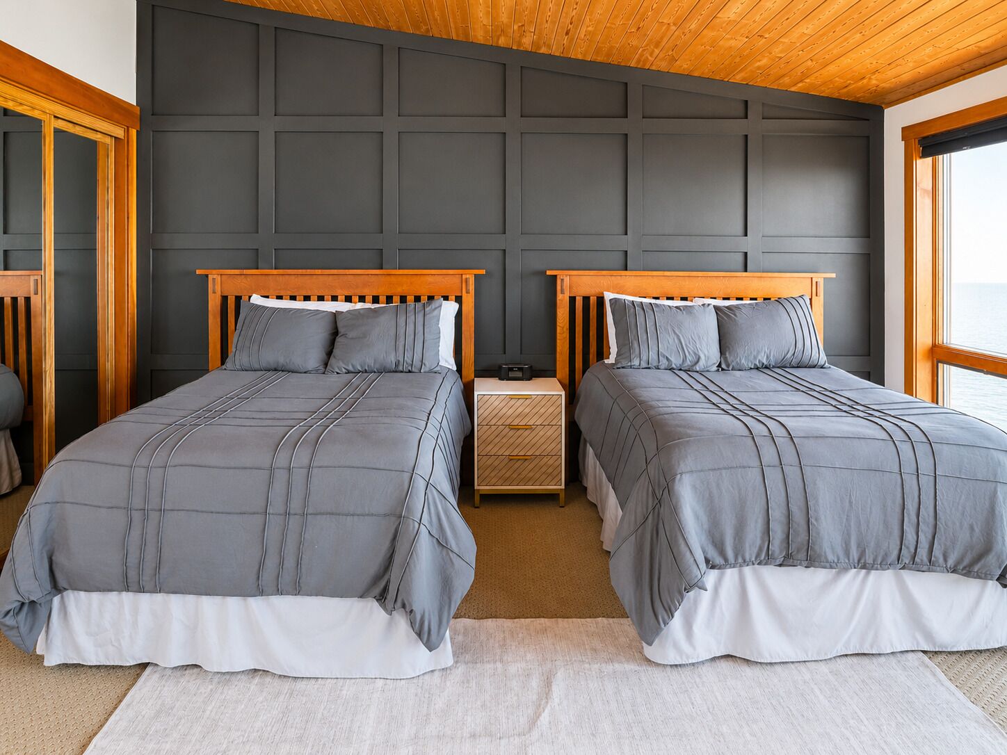 Una habitación con dos camas, techo de madera y un panel de pared oscuro.