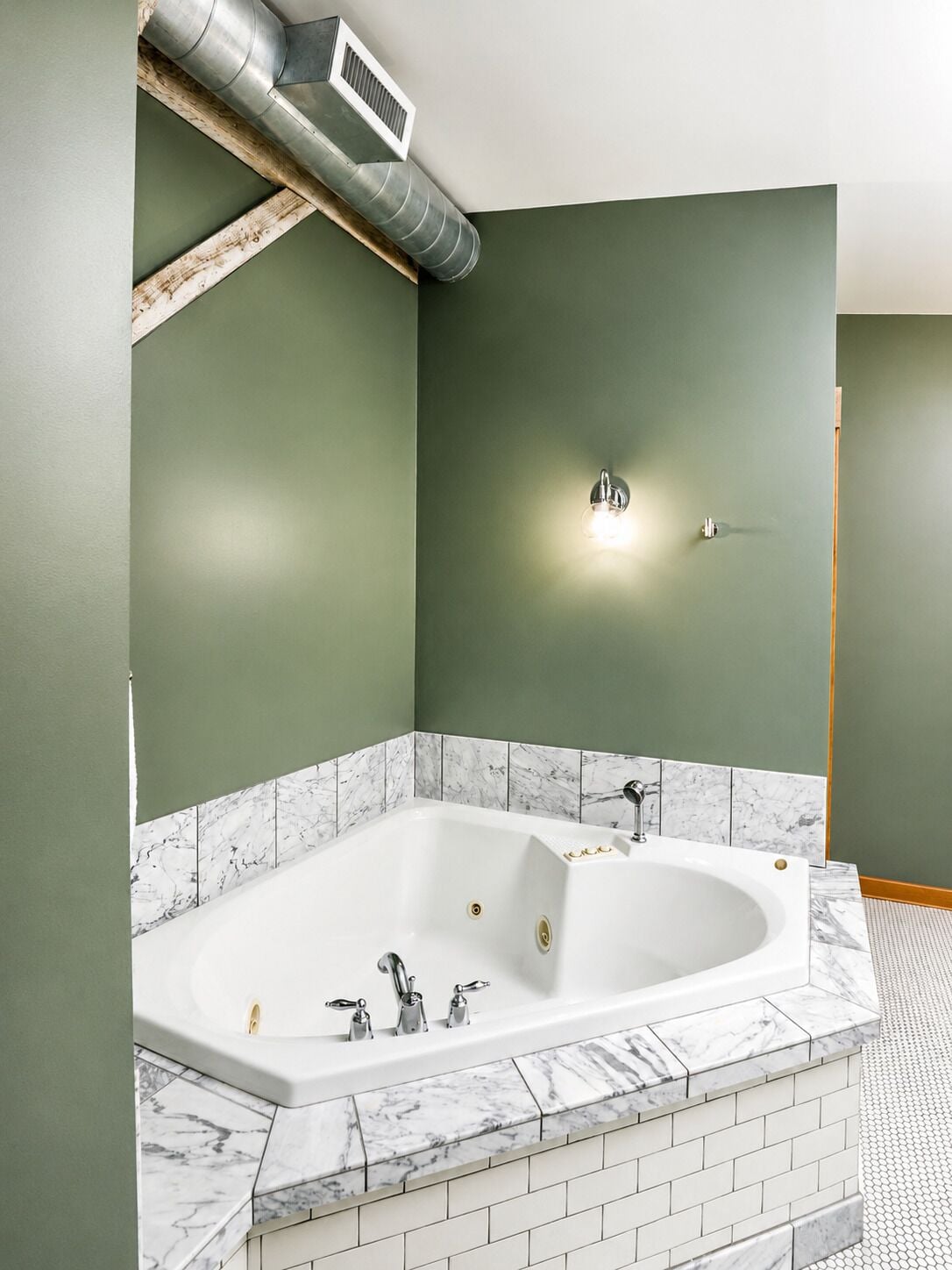 Un baño moderno con una bañera independiente, azulejos de mármol y una pared verde.