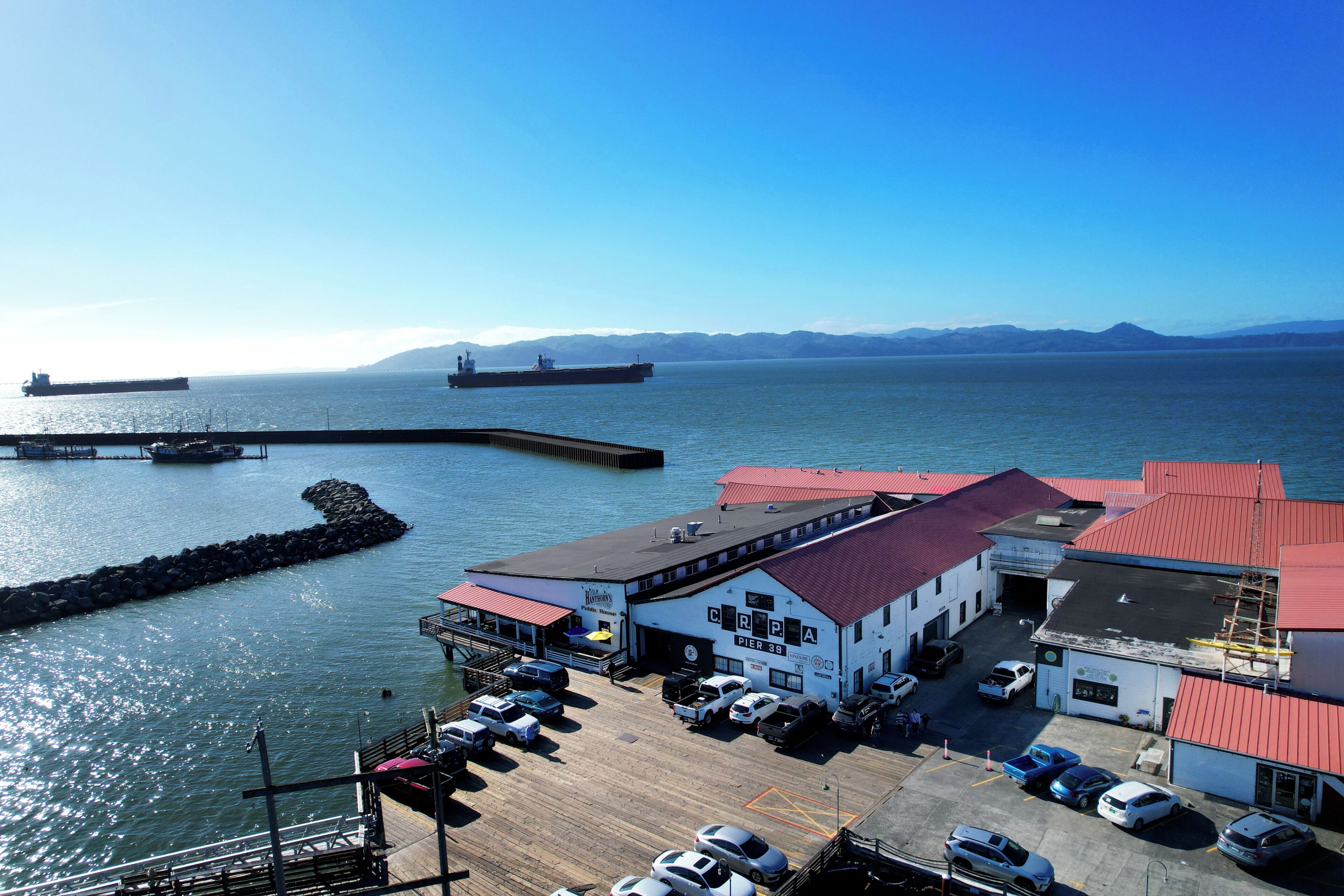 Un muelle con un barco amarrado, un edificio con techo rojo y un estacionamiento con coches.