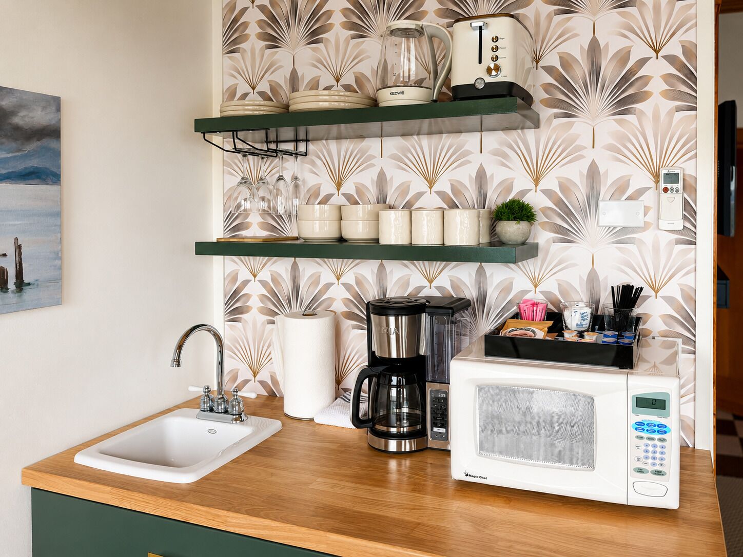 Una cocina con un lavamanos, cafetera, microondas y estantes con utensilios de cocina.