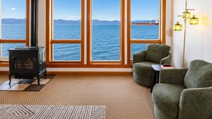 Una habitación con estufa de leña, vistas al mar y un sillón verde.