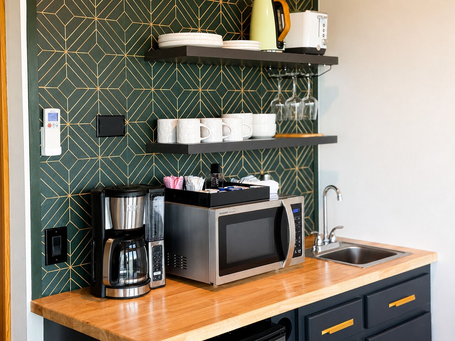 A modern kitchen with a microwave, coffee maker, and a coffee pot. There are shelves above the counter holding plates, cups, and a toaster.