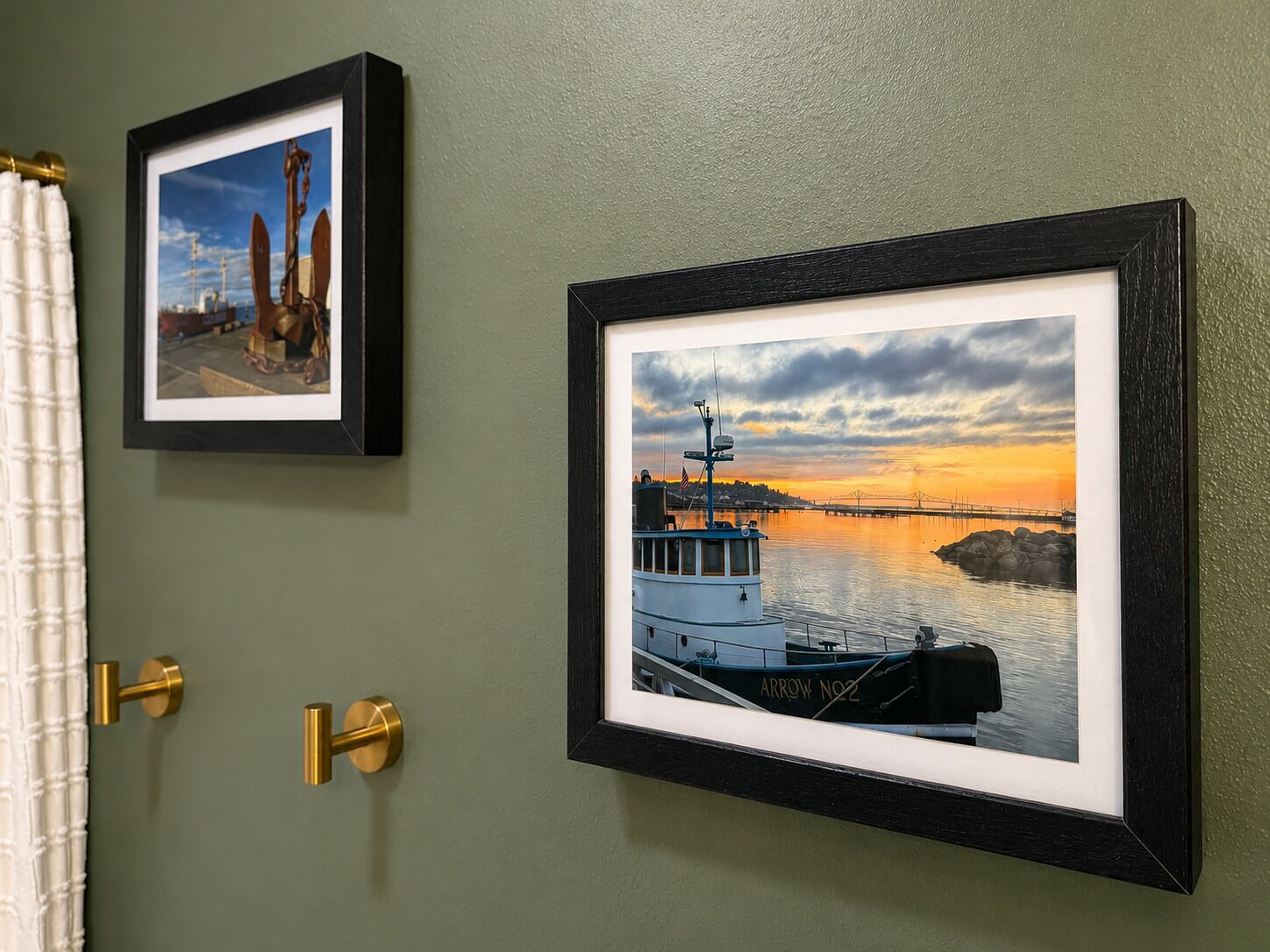 Dos fotografías enmarcadas en una pared, una que muestra un barco y otra con una escena de atardecer.