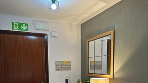 Una habitación con puerta de madera, un espejo, una lámpara, una planta, un teléfono y un aplique.