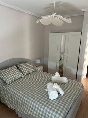 Ein Schlafzimmer mit einem Bett, karierten Bettwäsche, einem Deckenventilator, einem Nachttisch, einer Lampe, einem Kleiderschrank und Handtüchern.