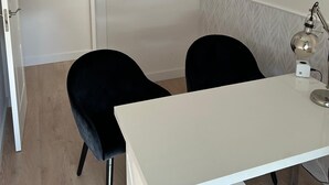 Una habitación con un escritorio blanco, dos sillas negras, una lámpara colgante y una puerta.