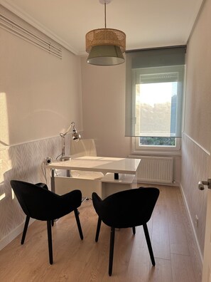 Ein modernes Zimmer mit einem weißen Schreibtisch, zwei schwarzen Stühlen, einer Pendelleuchte und einem Fenster mit Blick.
