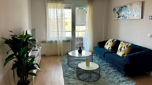 Una sala de estar con un sofá azul, una mesa de centro redonda, una planta en maceta y un cuadro en la pared.