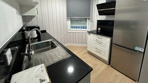 Una cocina moderna con un refrigerador de acero inoxidable, una encimera negra, un horno empotrado y una ventana con persianas.