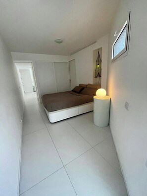 Un dormitorio con cama, lámpara de noche, una puerta y una lámpara fijada a la pared.