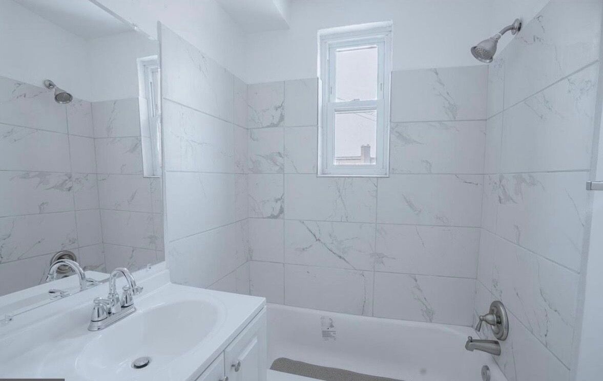 A bathroom with a double sink, a bathtub, a shower, and a window.