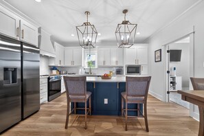 A modern kitchen with white cabinets, stainless steel appliances, and two pendant lights. - Canal Front House with Dock and Outdoor Area (Bay St. Louis)