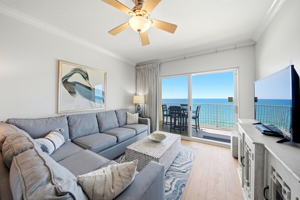 Ein Wohnzimmer mit Sofa, Couchtisch, Deckenventilator, Fernseher und einem Balkon mit Meerblick.