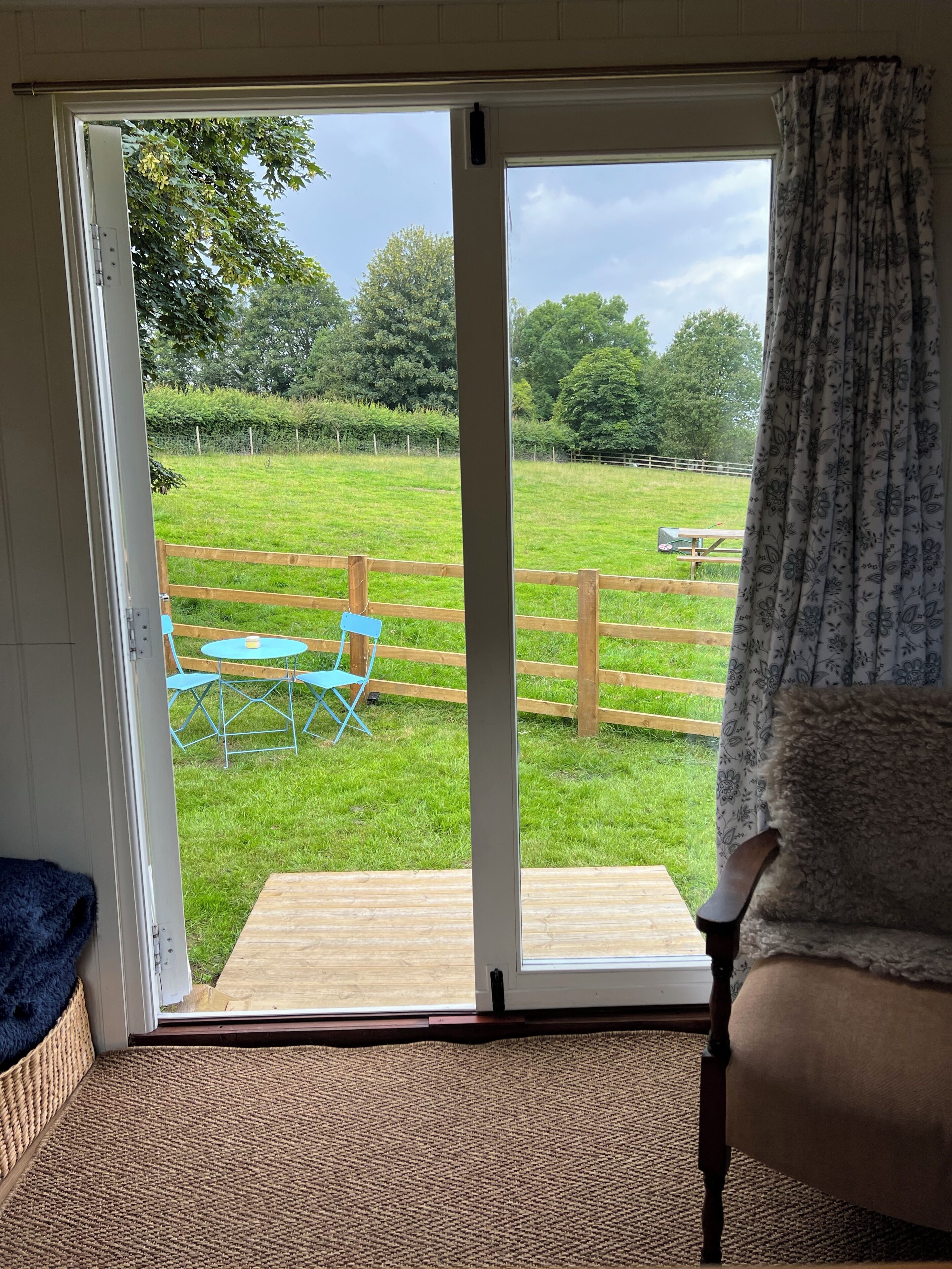 A room with a sliding glass door leading to a grassy outdoor area with a wooden deck, a blue chair, and a table.