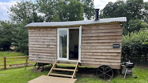 En hyggelig træhytte med skydedør, lille veranda, bord og stole.