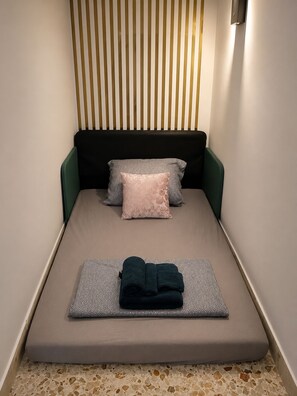 A small, single-bed room with a slatted headboard, patterned pillows, and a folded towel on the bed. - Cinema Apartment • 5 Guests • Near Beach Trapani (Sicily)
