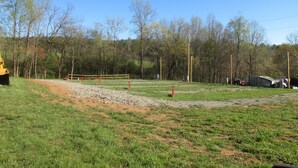 A rural landscape with a dirt path, a yellow construction vehicle, and a fenced area with trees in the background.