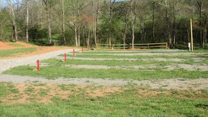 A fenced outdoor area with a gravel path, trees, and a grassy field.