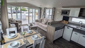 A modern kitchen with a dining area, large windows, and a view of parked cars outside. - 025 Maes Glas (Holywell)