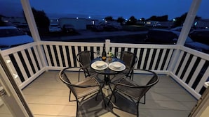 A covered outdoor seating area with a table and chairs, a bottle of wine, and a bowl. - 025 Maes Glas (Holywell)