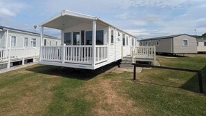 A mobile home with a covered porch, a fenced yard, and a grassy area. - 025 Maes Glas (Holywell)