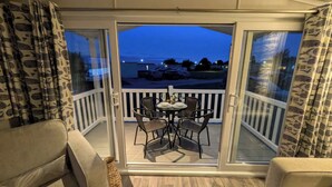 A balcony with a table and chairs, a view of the sea, and a building in the background. - 025 Maes Glas (Holywell)