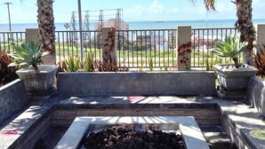 An outdoor seating area with a fire pit, surrounded by palm trees and a view of the ocean. - Beautiful 4 bedroom vacation home in Punta Azul (Rosarito)