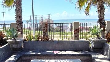 An outdoor seating area with a fire pit, surrounded by palm trees and a view of the ocean.