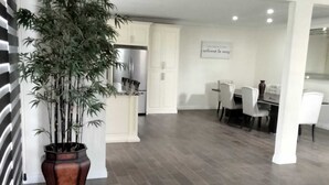A modern kitchen with white cabinets, a large potted plant, and a dining area with white chairs and a table. - Beautiful 4 bedroom vacation home in Punta Azul (Rosarito)
