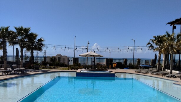 A rectangular swimming pool with clear blue water, surrounded by palm trees and lounge chairs. - Beautiful 4 bedroom vacation home in Punta Azul (Rosarito)