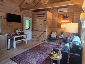 Interior de una cabaña de madera con comedor, sofá, lámpara y alfombra.