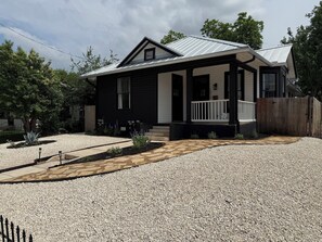 Ein Bungalow mit Veranda, einem Schotterweg und einem Holzzaun.