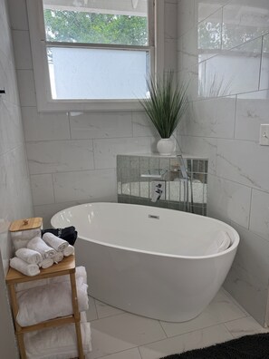 Ein modernes Badezimmer mit freistehender Badewanne, einem Fenster mit Blick auf Grünflächen und einer kleinen Pflanze auf dem Fensterbrett.