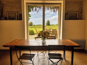 Ein Esstisch mit Stühlen, eine Blumenvase und Blick ins Freie durch eine Tür.