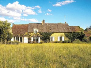 Ein zweistöckiges Haus mit Ziegeldach und einer Veranda, davor ein großes Feld.