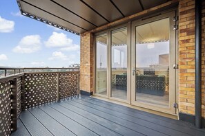 Ein Balkon mit Holzboden, Glastür und Backsteinwand.