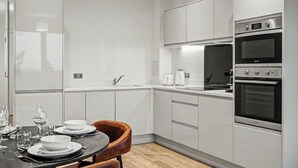 Uma cozinha moderna com armários brancos, eletrodomésticos de aço inoxidável e um espaço de jantar com mesa posta para quatro pessoas.