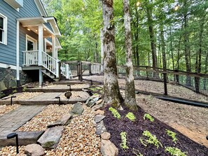 A house with a porch, a stone wall, and a forested area with a fence. - Luxury Home, Gorgeous Wooded Mountain Views, Pet Friendly, SLEEPS 10 (Ellijay)