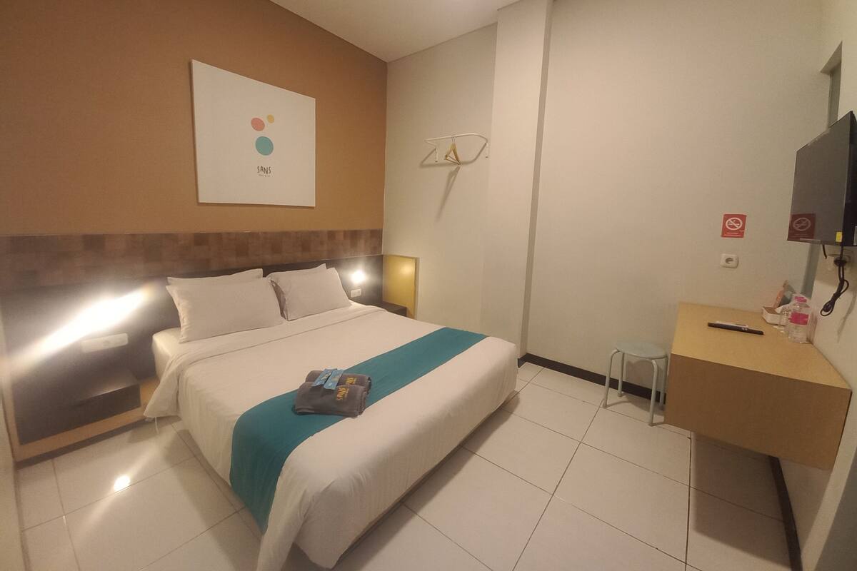 Hotellihuone, jossa on sänky, työpöytä, tuoli, televisio ja seinälle ripustettu taideteos.